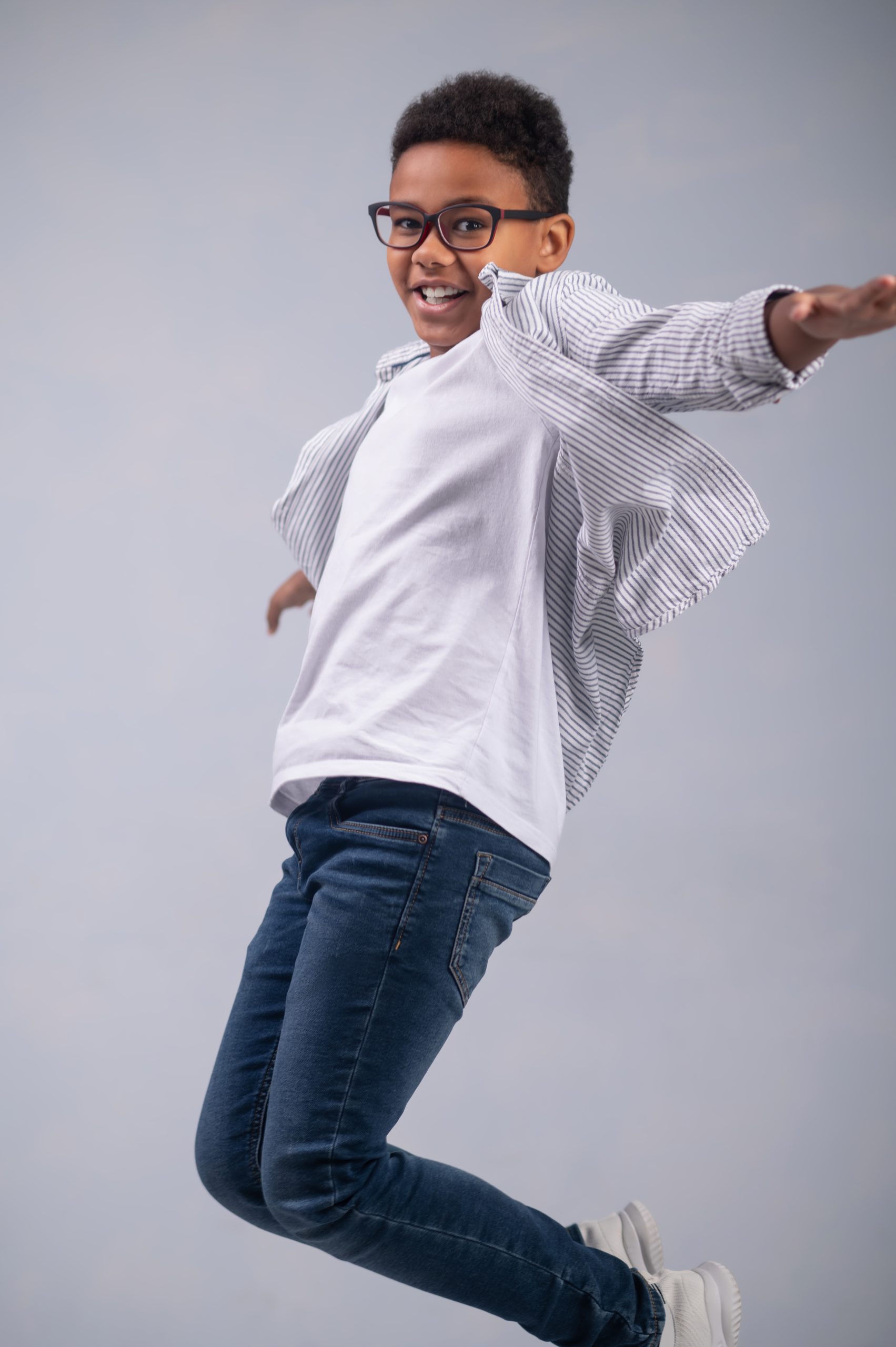 Smiling pleased African American boy in stylish eyeglasses leaping into the air before the camera
